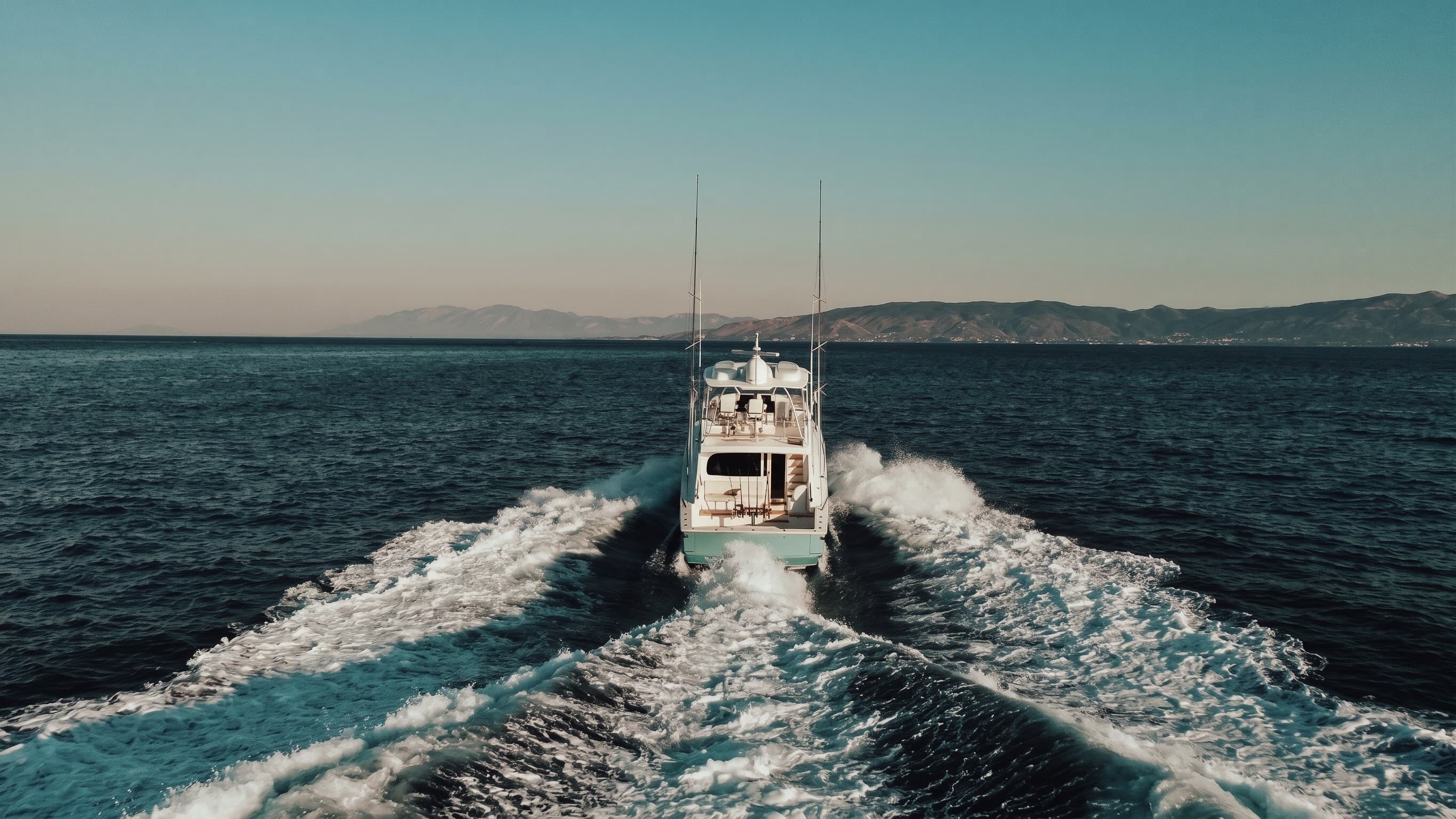 A sportfishing yacht under way, seen from astern with its wake behind it